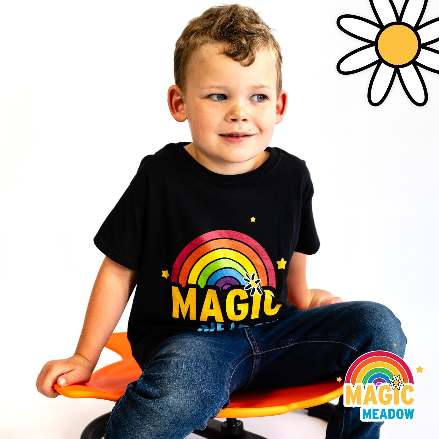 Young boy sitting on an orange Spinning Fish sensory seat. Child looks off to the right while holding the fins of the fish. Feet placed on the floor. Child wears blue jeans with black tshirt showing MagicMeadow logo.
Daisy graphic in top right corner. MagicMeadow in bottom left corner.