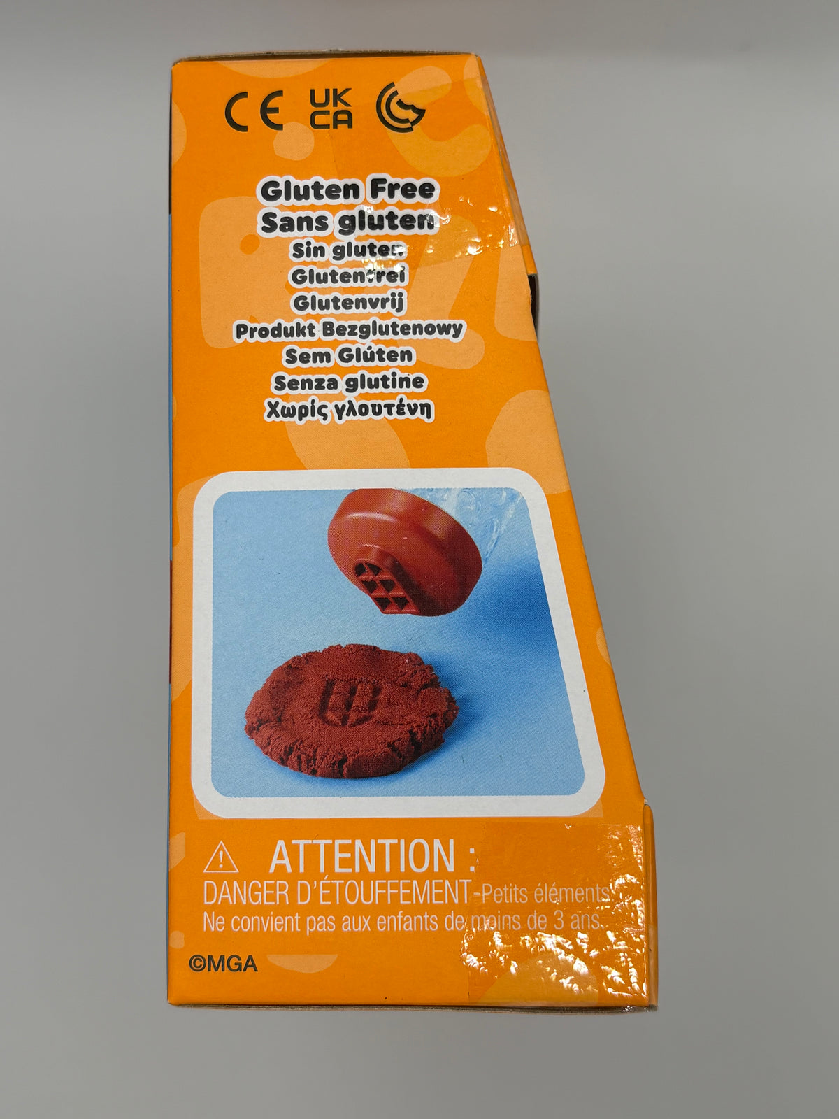 An orange box of gluten-free round cookies, featuring text in multiple languages and a photo of the reddish-brown cookies on a blue background.
