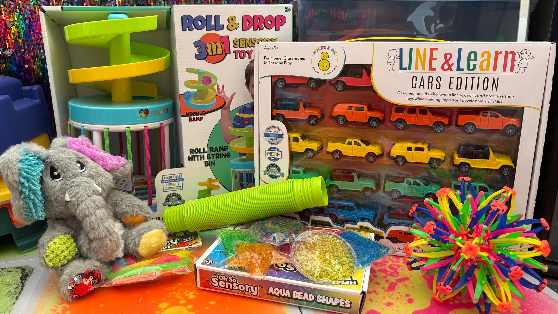 Assorted children's toys and educational materials on a colorful surface with a textured wall background.
