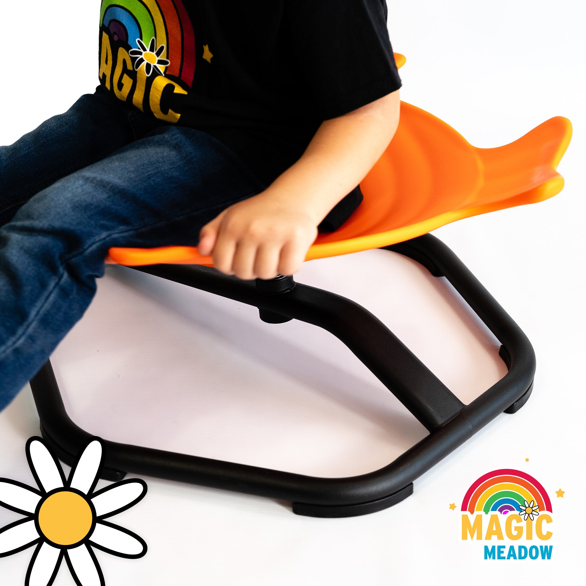 child in blue jeans with black MagicMeadow logo tshirt, sat on an orange Spinning Fish seat. View focused on the black hexagon base of the sensory spinning seat toy. 
White daisy image bottom left corner. MagicMeadow Rainbow and daisy logo bottom right corner.