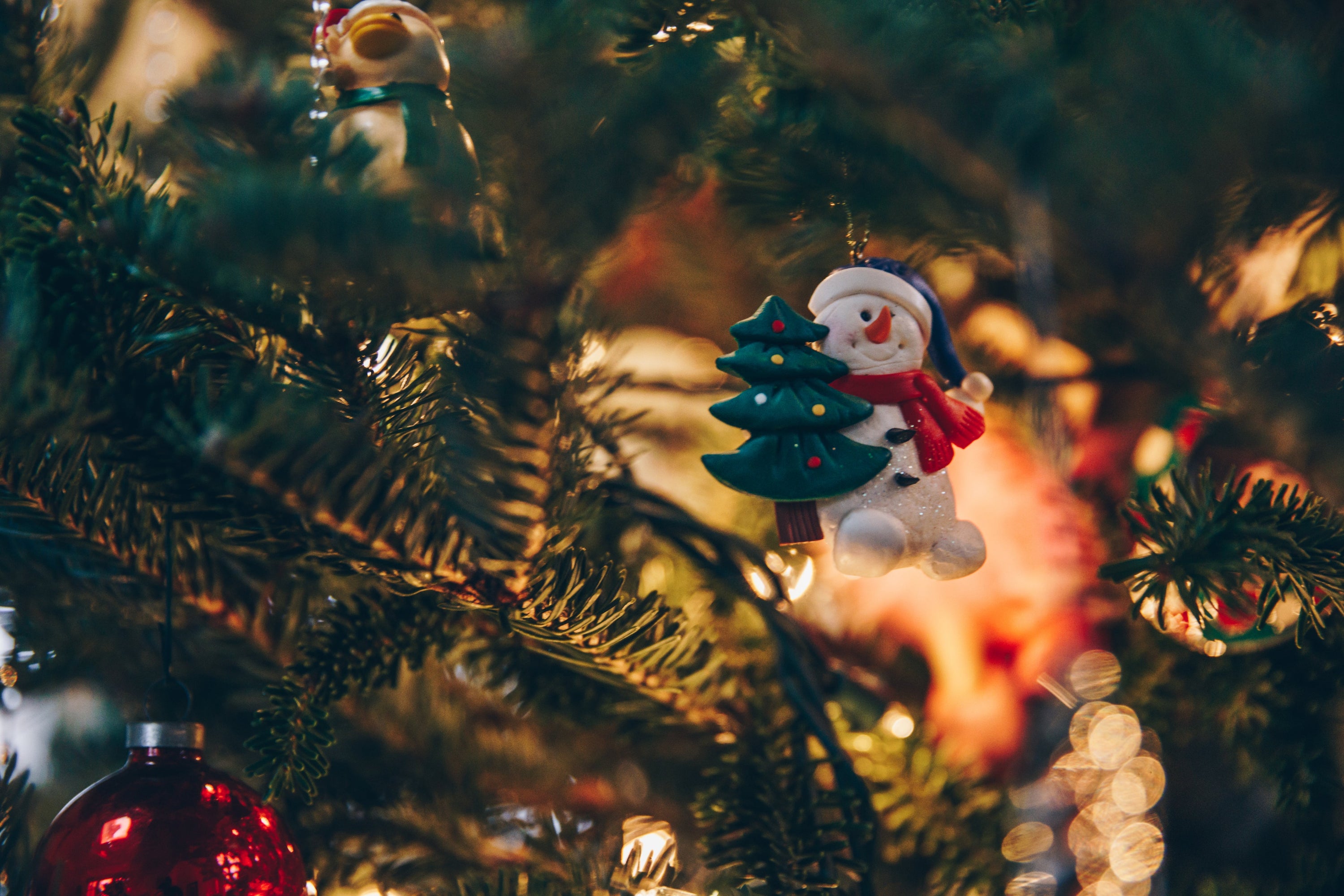 close up of snowman and christmas tree ornament on a real fir tree with soft warm lighting. 